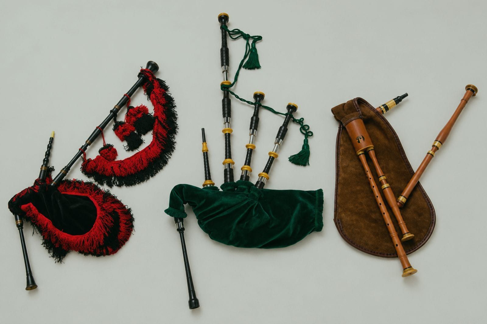 Tres gaitas de fol distintas alineadas sobre fondo claro: una con flecos granate y negro, una escocesa de fuelle verde con borlas, y una de madera natural con su funda